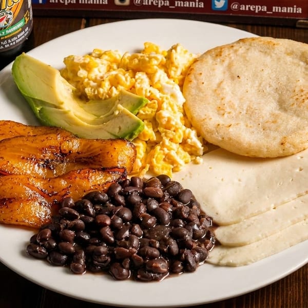 Plate with scrambled eggs, avocado, fried plantains, black beans, arepa, and white cheese.
