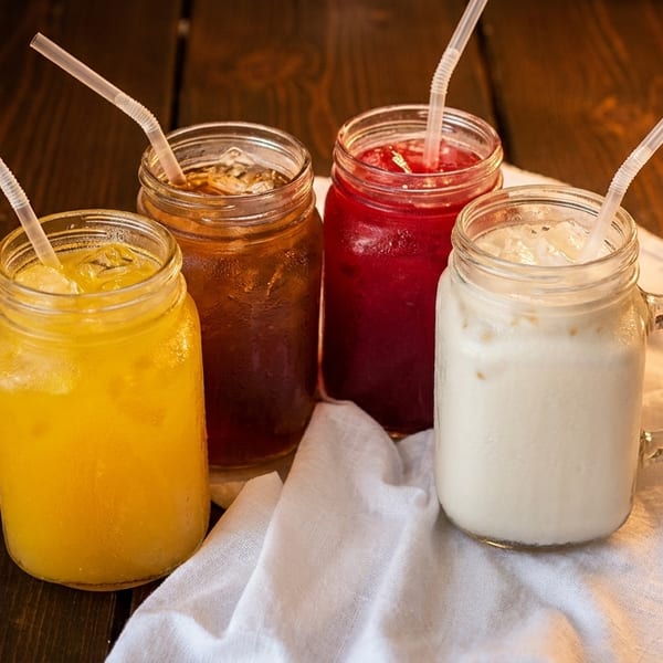 Four iced drinks in mason jars with straws on a rustic wooden table.