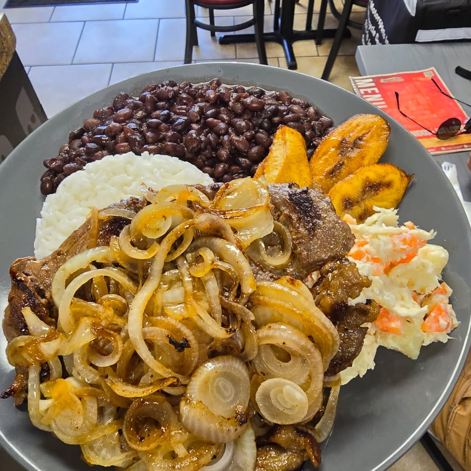 Bistec encebollado with sauteed onions, rice, beans and plantains.