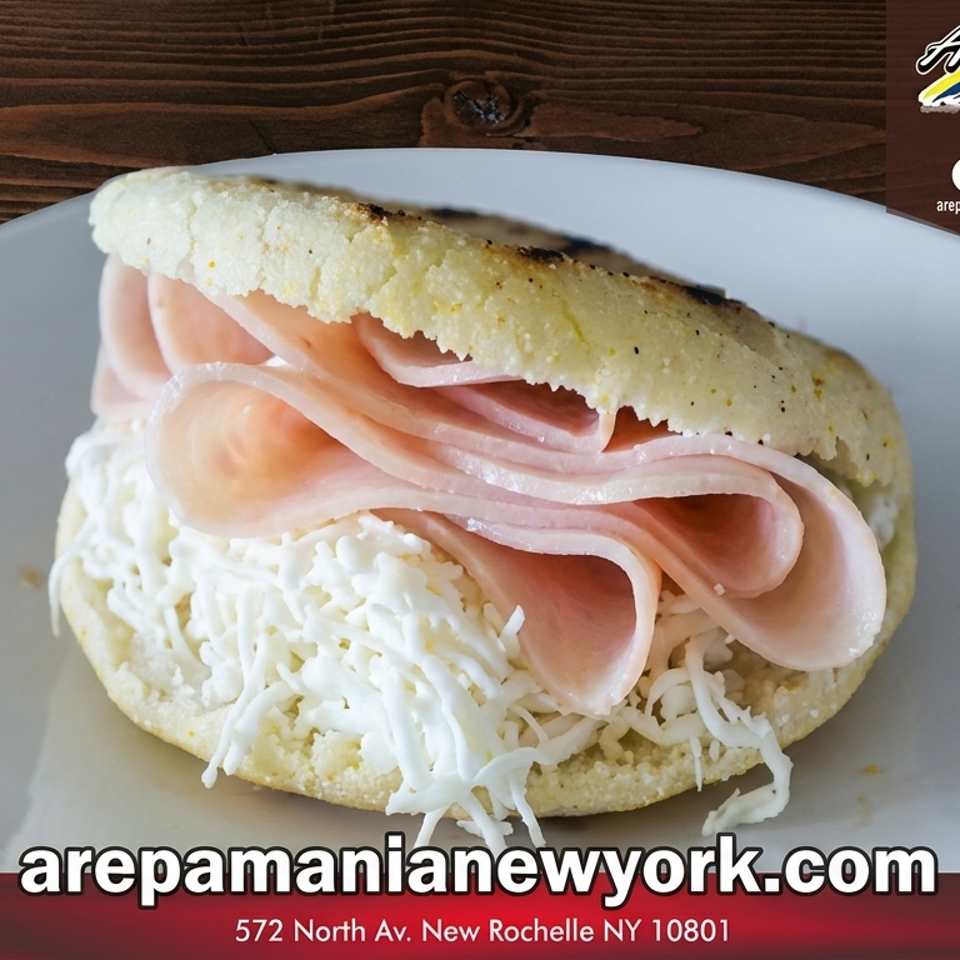 A golden arepa filled with thinly sliced ham and shredded white cheese on a white plate.